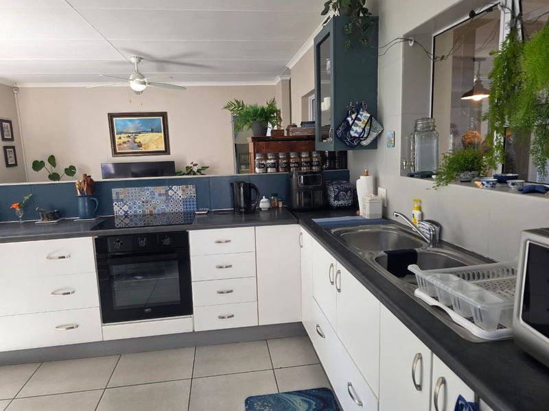 An open-plan kitchen featuring white cabinetry, dark countertops, a built-in oven, electric hob, and a double bowl sink, seamlessly connected to the living area.