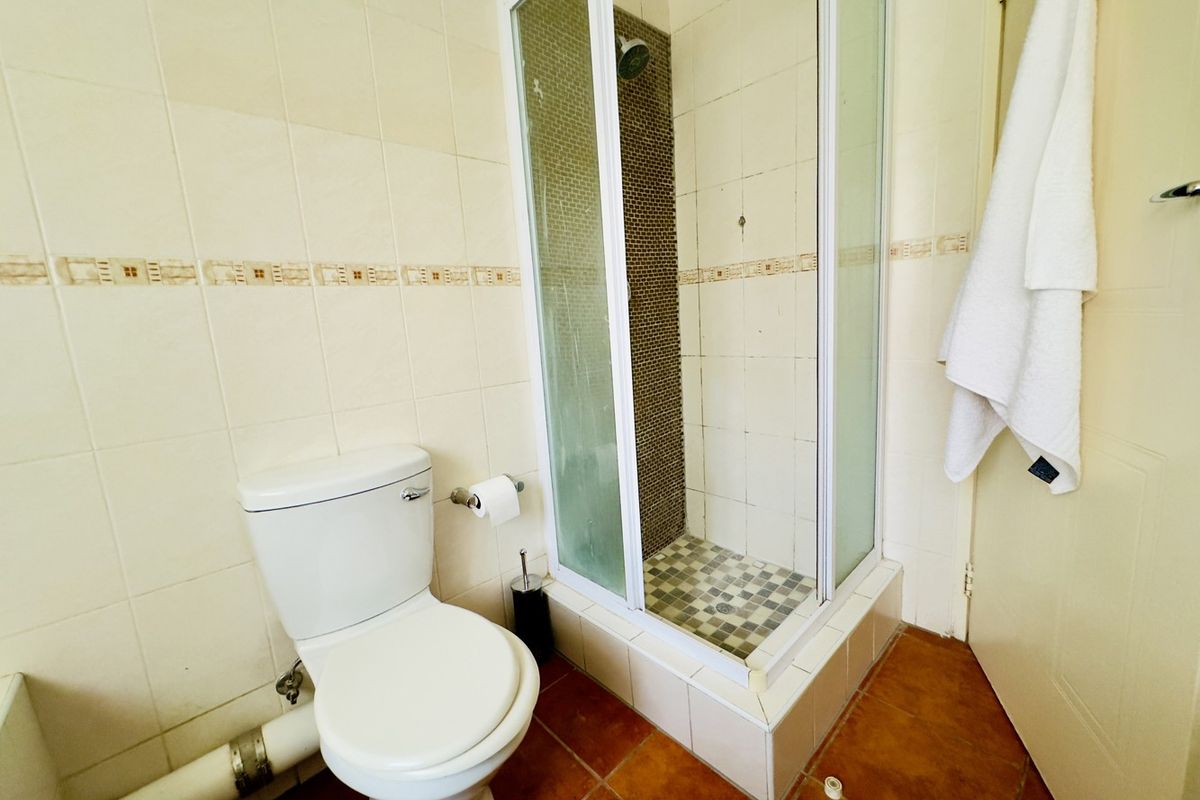 A functional bathroom featuring a corner shower enclosure, ceramic tiling, and a standard toilet, currently showing signs of wear and dated finishes.