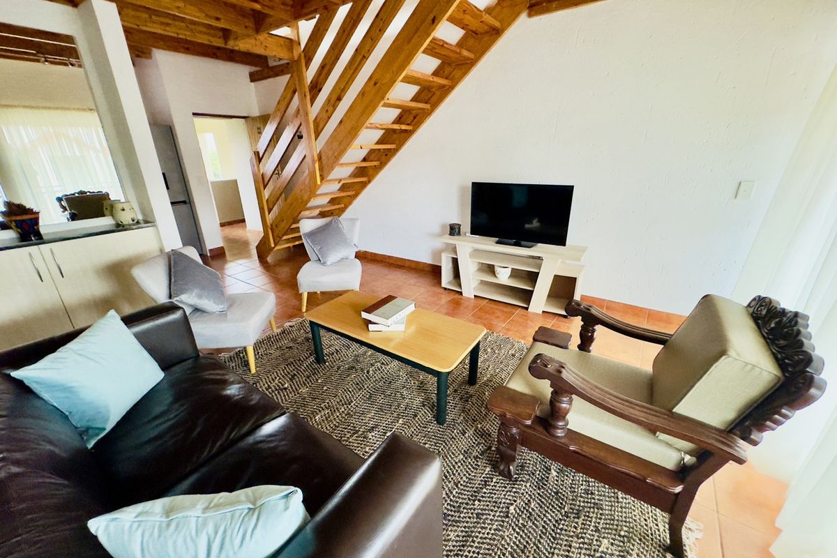 Open-plan living area featuring exposed timber staircase and ceiling beams with terracotta floor tiles.