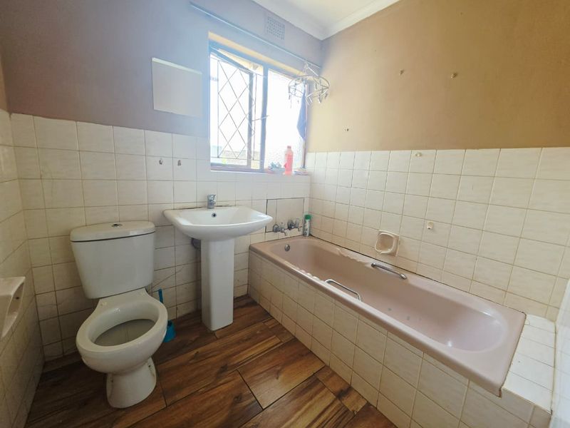 A dated bathroom featuring a pedestal basin, toilet, and bathtub with tiled walls, requiring cosmetic updates to modernize the space.