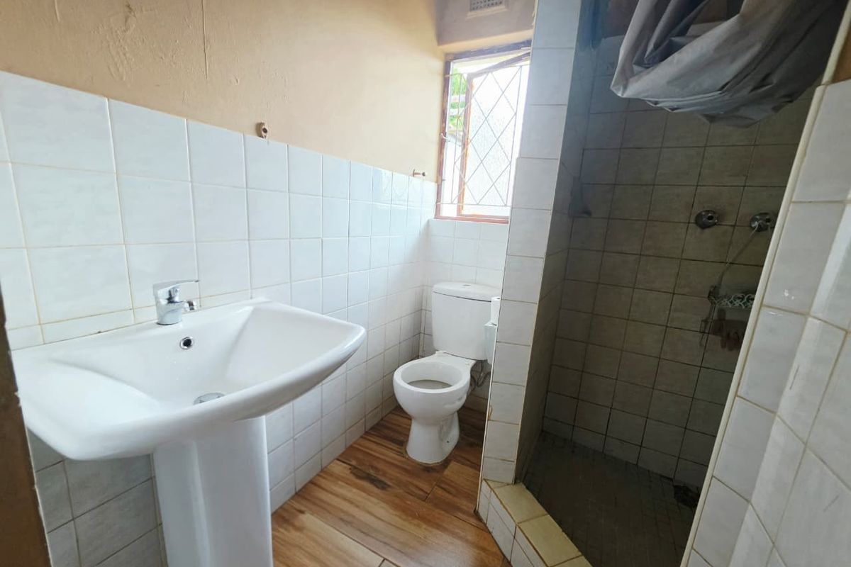 A functional bathroom featuring a pedestal basin, toilet, and a tiled shower enclosure with wood-look floor tiles.