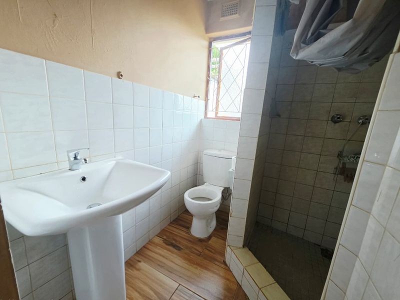 A functional bathroom featuring a pedestal basin, toilet, and a tiled shower enclosure with wood-look floor tiles.