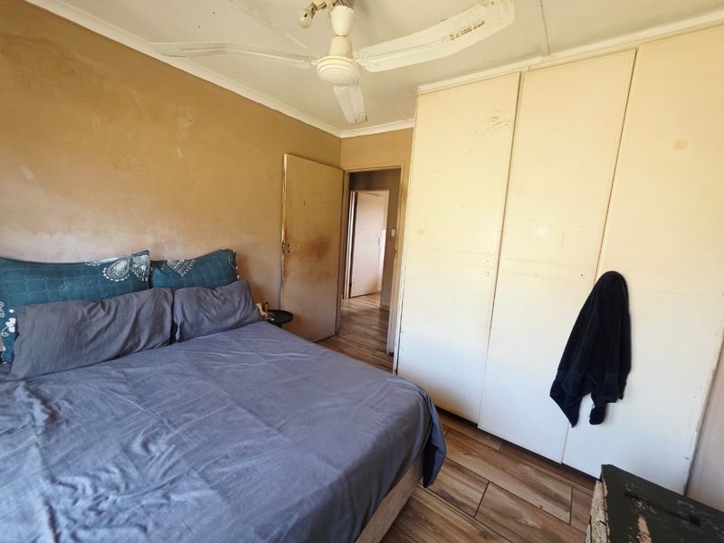 A bedroom featuring built-in cupboards, a ceiling fan, and tiled flooring. The room requires cosmetic updates to the walls and finishes.