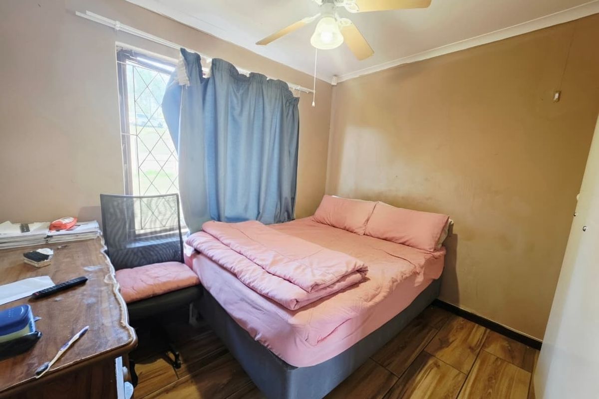 A compact bedroom featuring tiled flooring and a ceiling fan, currently showing signs of wear on the wall surfaces.