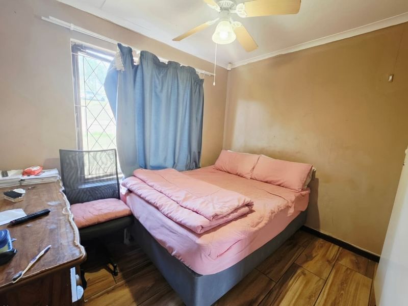 A compact bedroom featuring tiled flooring and a ceiling fan, currently showing signs of wear on the wall surfaces.