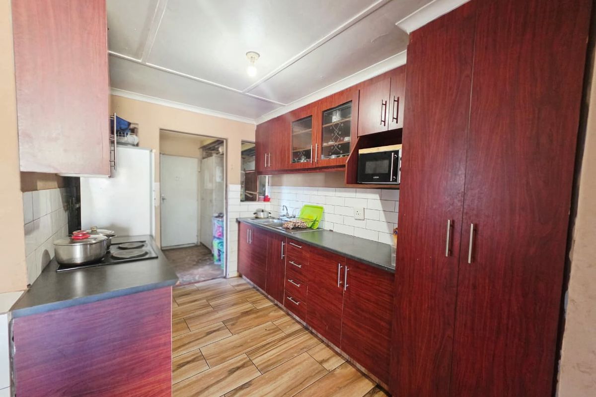 A functional kitchen featuring wood-look cabinetry, dark laminate countertops, a tiled backsplash, and built-in cooking appliances with tiled flooring throughout.