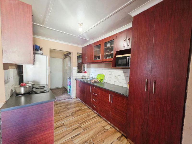 A functional kitchen featuring wood-look cabinetry, dark laminate countertops, a tiled backsplash, and built-in cooking appliances with tiled flooring throughout.