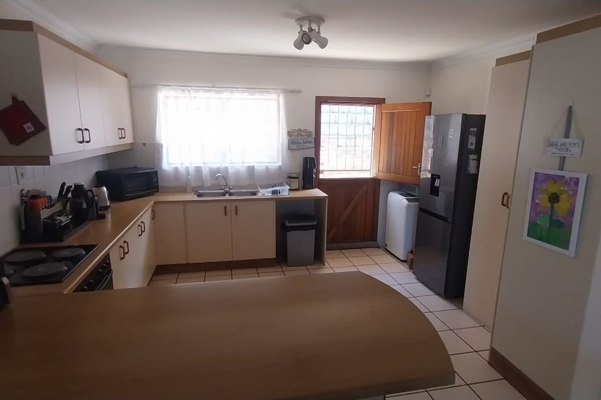 A functional kitchen featuring built-in cabinetry, laminate countertops, a double bowl sink, electric hob, and tiled flooring with direct access to the exterior.