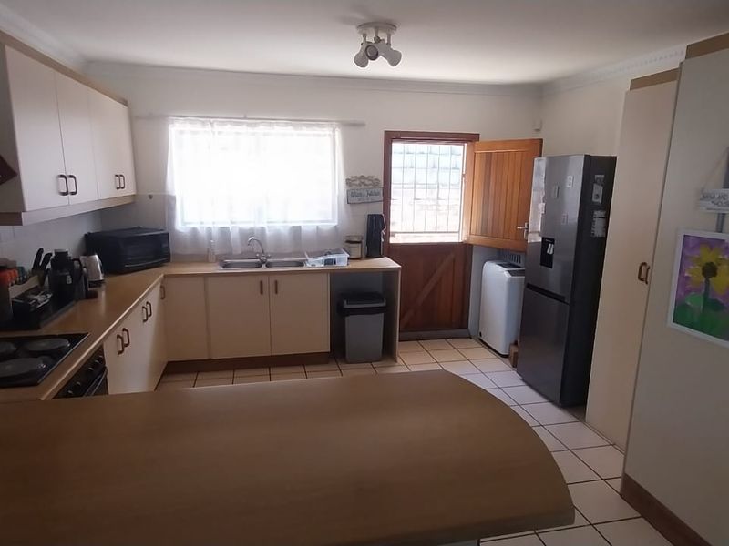 A functional kitchen featuring built-in cabinetry, laminate countertops, a double bowl sink, electric hob, and tiled flooring with direct access to the exterior.