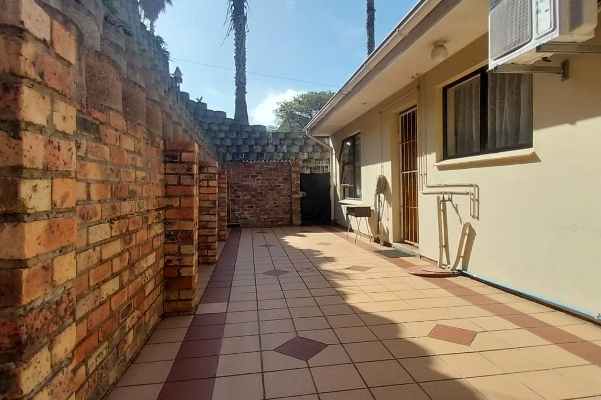 A paved rear patio area featuring a brick retaining wall, security gate, and external air conditioning unit.