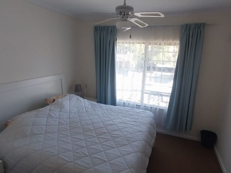 A standard bedroom featuring a ceiling fan and a large sliding window with curtains, providing natural light and ventilation.