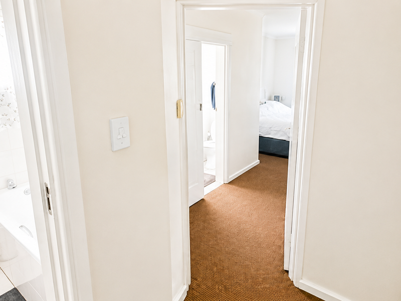 A view from the hallway looking into a bathroom with a bathtub and toilet, with a bedroom visible in the background.