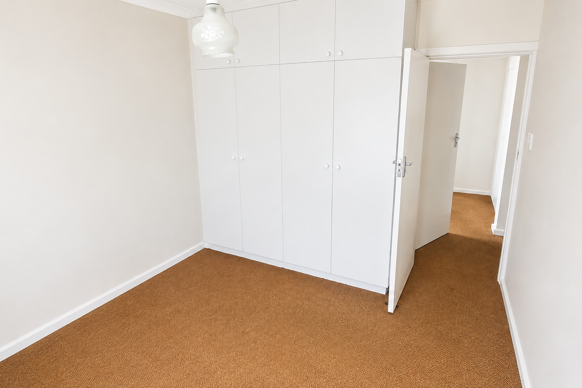 A clean, empty bedroom featuring neutral walls, brown carpet flooring, and ample built-in cupboard storage space.
