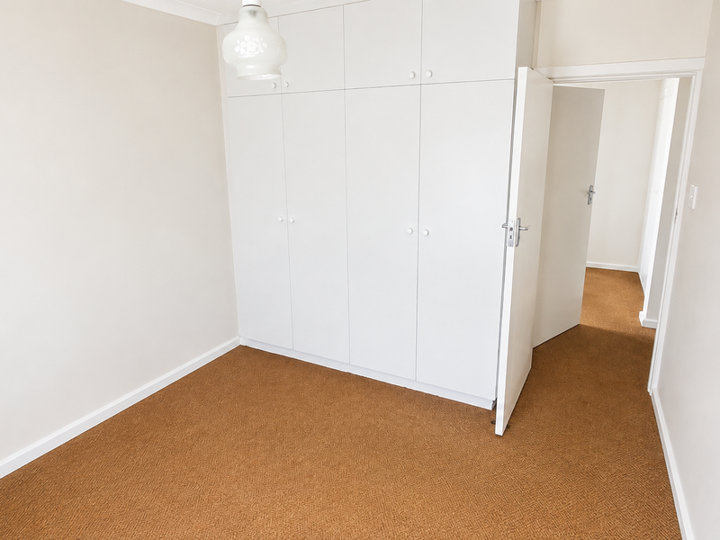 A clean, empty bedroom featuring neutral walls, brown carpet flooring, and ample built-in cupboard storage space.