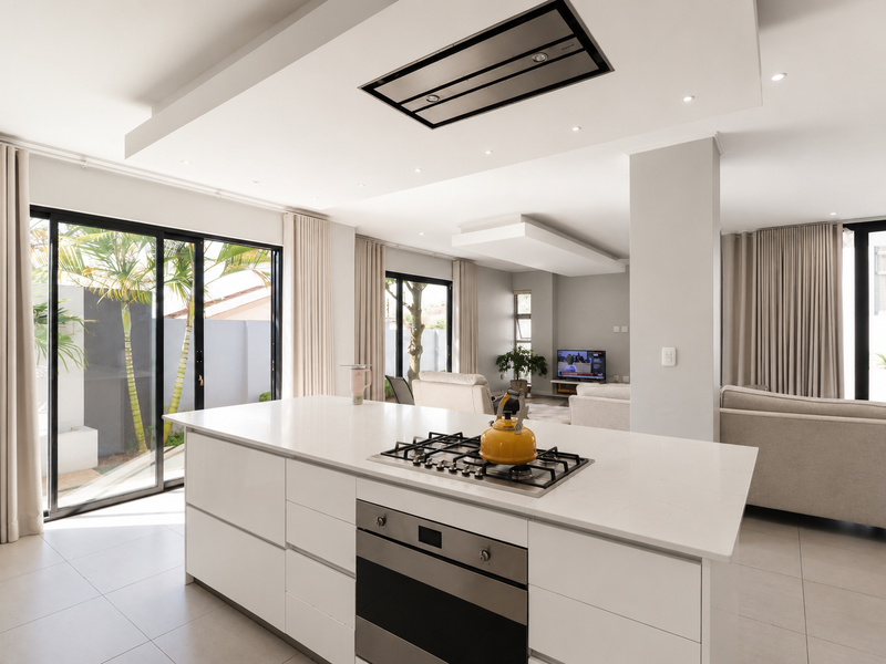 Modern open-plan kitchen and living area featuring a central island with gas hob, built-in oven, sleek cabinetry, and large sliding doors leading outdoors.