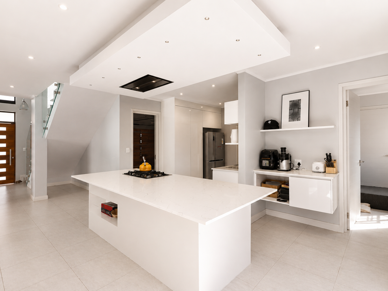 Modern open-plan kitchen featuring a large central island with quartz countertops, gas cooktop, sleek cabinetry, and recessed lighting in a contemporary drop ceiling.