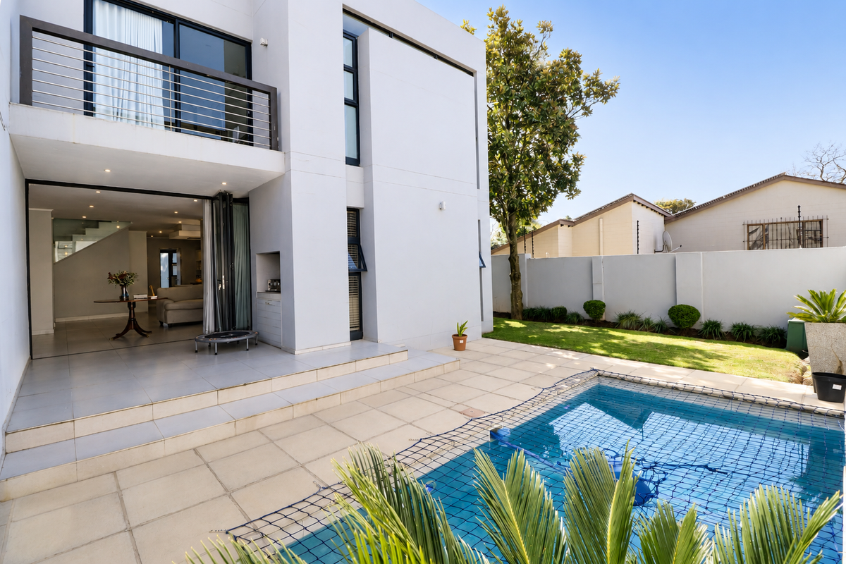 Modern rear exterior featuring a tiled patio, swimming pool with safety net, and a balcony overlooking the garden and pool area.