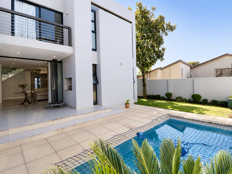 Modern rear exterior featuring a tiled patio, swimming pool with safety net, and a balcony overlooking the garden and pool area.