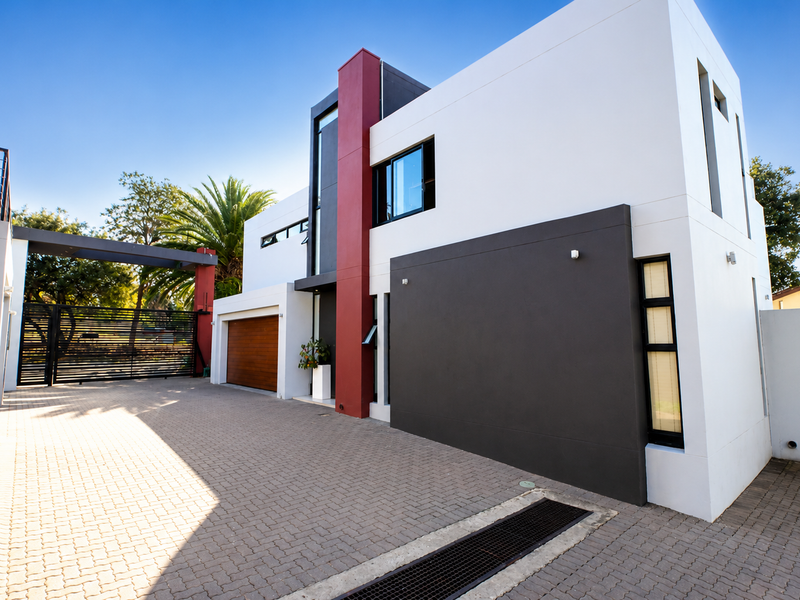 Modern double-story residential home featuring a clean architectural facade, paved driveway, and secure gated entrance.