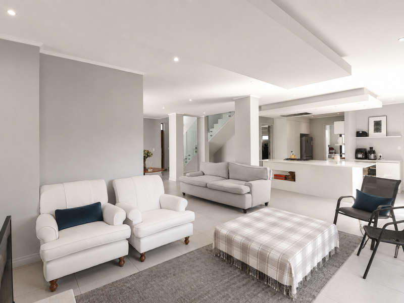 Spacious open-plan living area featuring a modern kitchen with island, recessed ceiling lighting, and a contemporary staircase with glass balustrade.