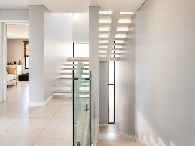 Modern hallway featuring a contemporary floating staircase with a sleek glass balustrade and neutral tiled flooring.