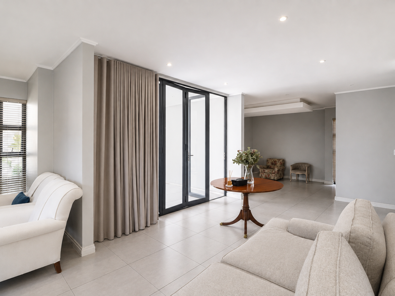 Spacious living area featuring neutral tiled flooring, recessed lighting, and large aluminium-framed glass doors providing seamless access to the outdoor space.