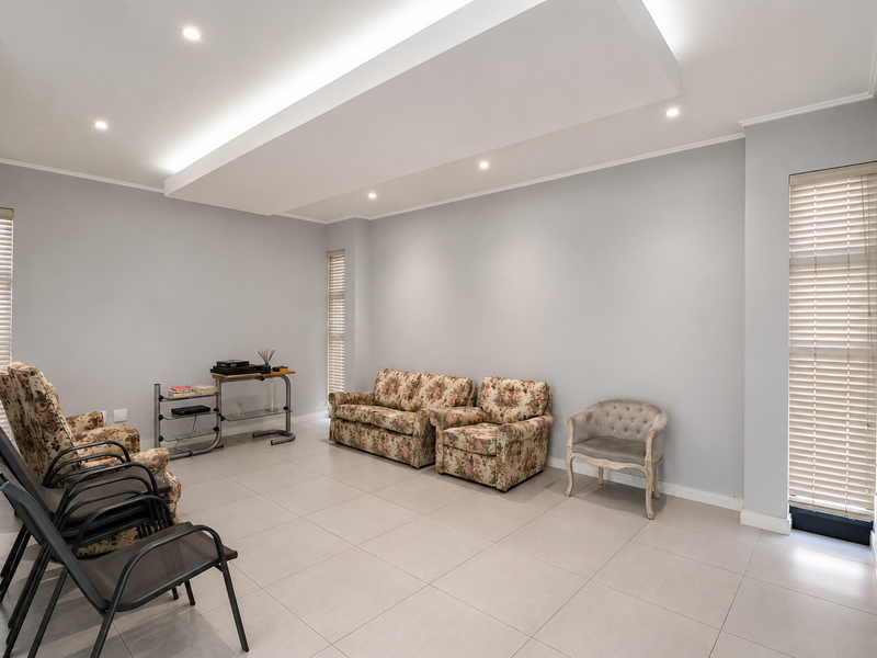 Spacious living room featuring neutral tiled flooring, a modern recessed ceiling with integrated downlighting, and large windows fitted with venetian blinds.