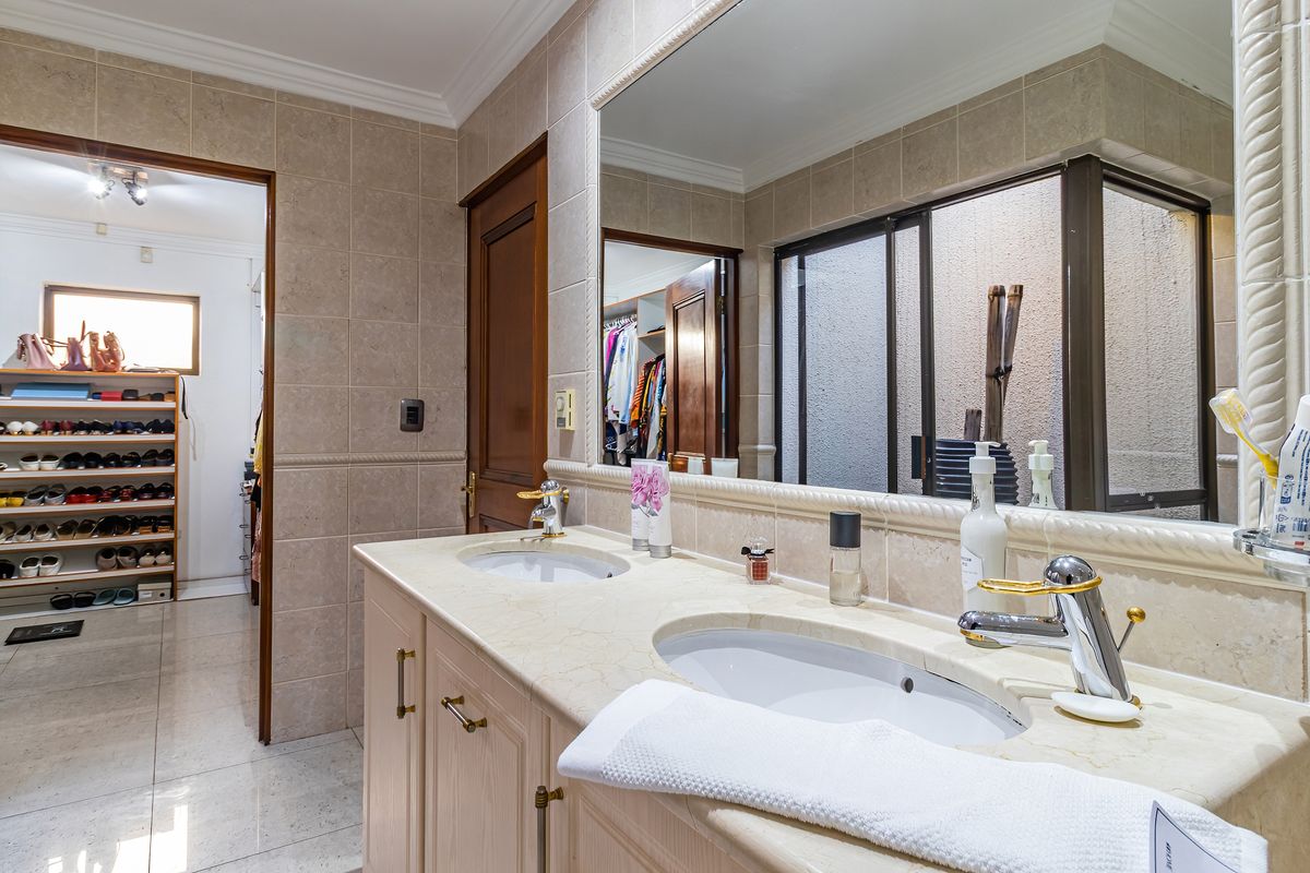 A well-maintained bathroom featuring a double vanity with stone countertops, chrome fixtures, and large wall-to-wall mirror, with an adjacent walk-in closet area.
