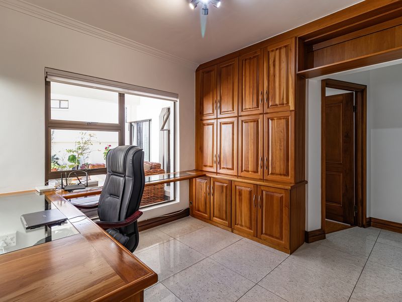 A well-appointed home office featuring extensive built-in wooden cabinetry, a matching integrated desk, tiled flooring, and large windows providing natural light.