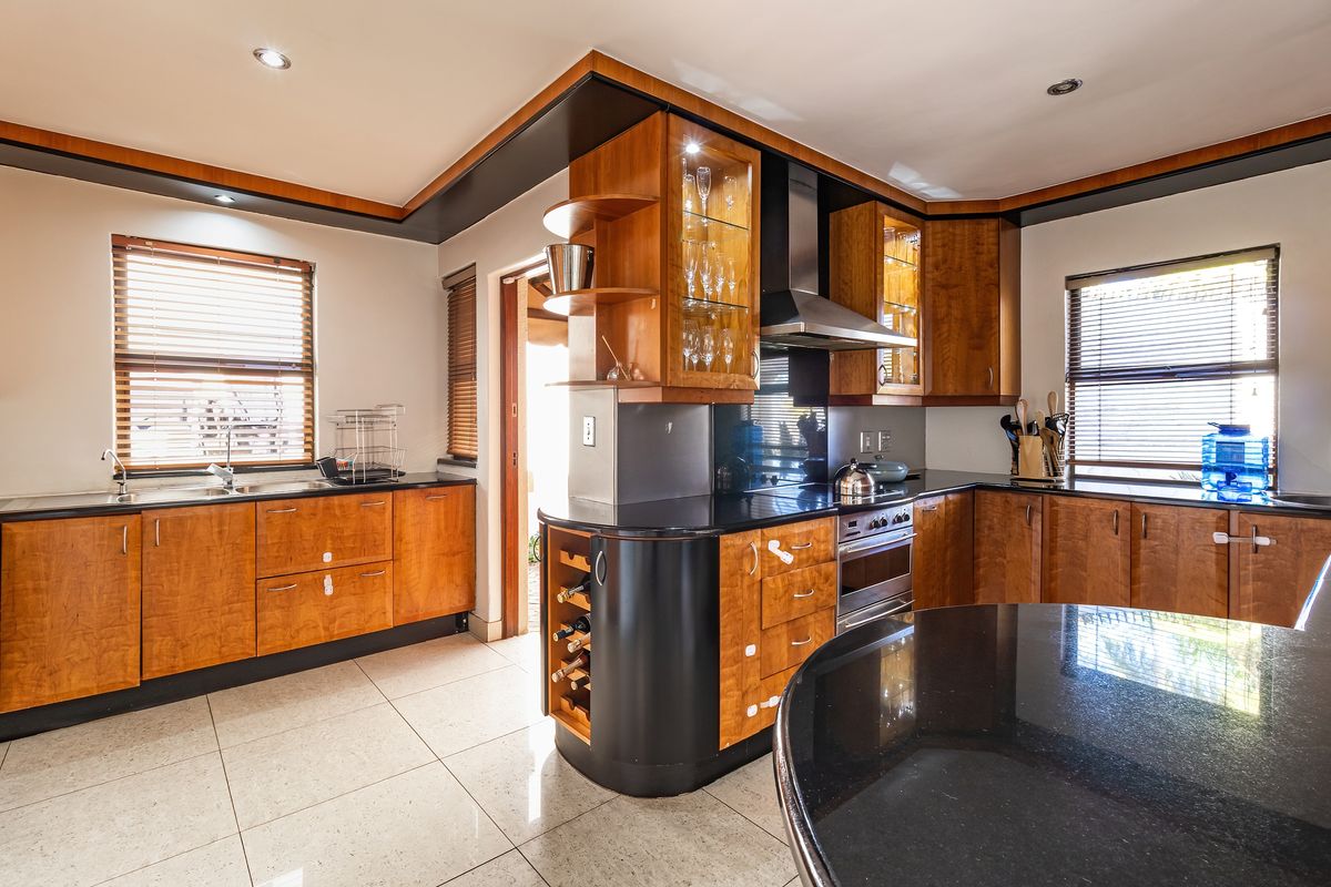 A well-appointed kitchen featuring warm-toned wooden cabinetry, contrasting black granite countertops, integrated appliances, and tiled flooring with ample natural light.