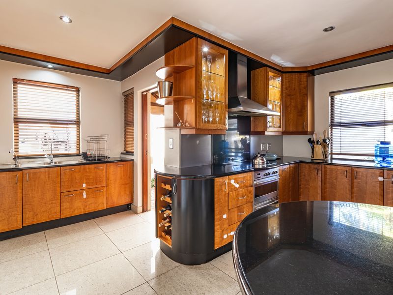 A well-appointed kitchen featuring warm-toned wooden cabinetry, contrasting black granite countertops, integrated appliances, and tiled flooring with ample natural light.