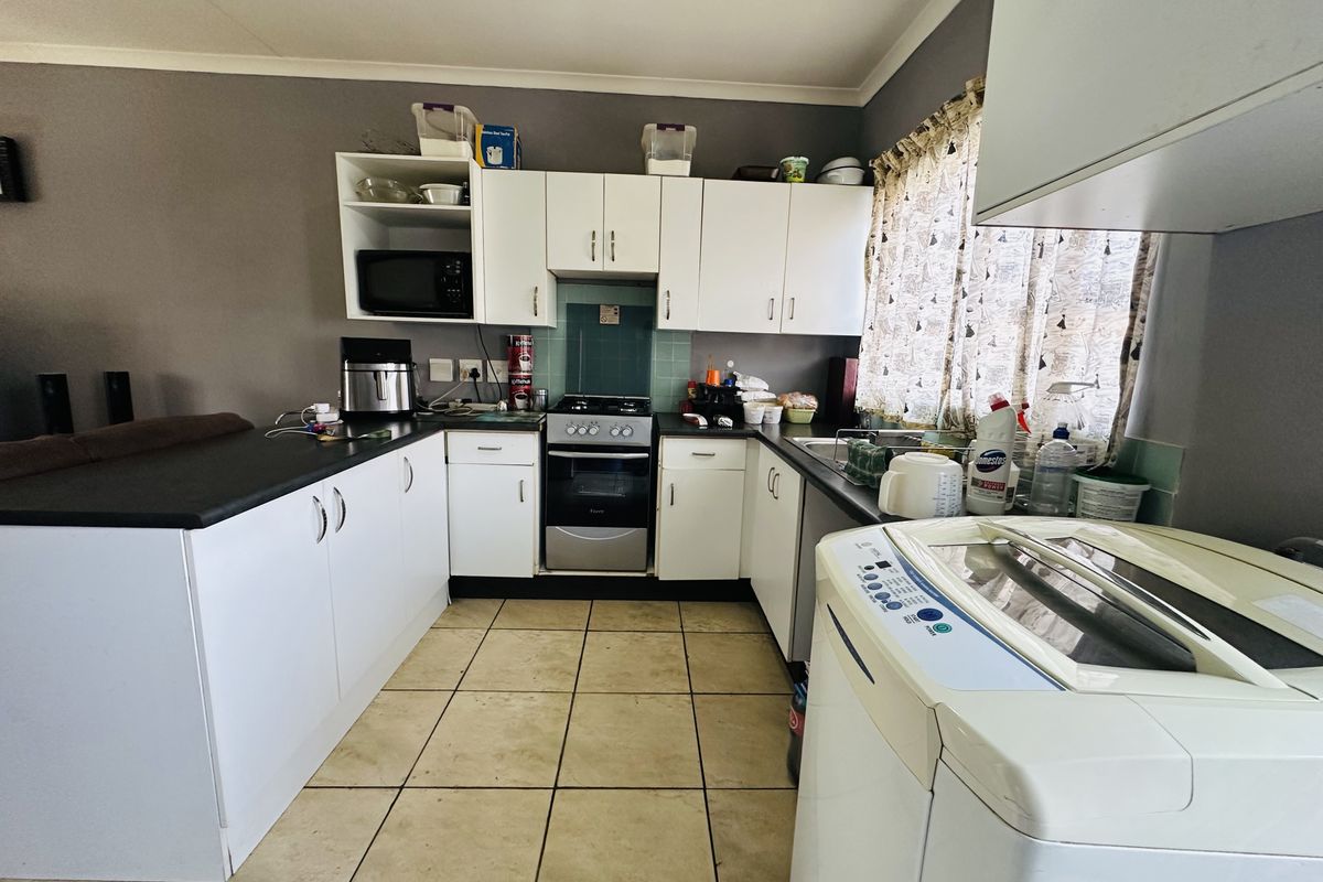 A functional kitchen featuring white cabinetry, dark laminate countertops, a freestanding oven, and tiled flooring with a practical layout.