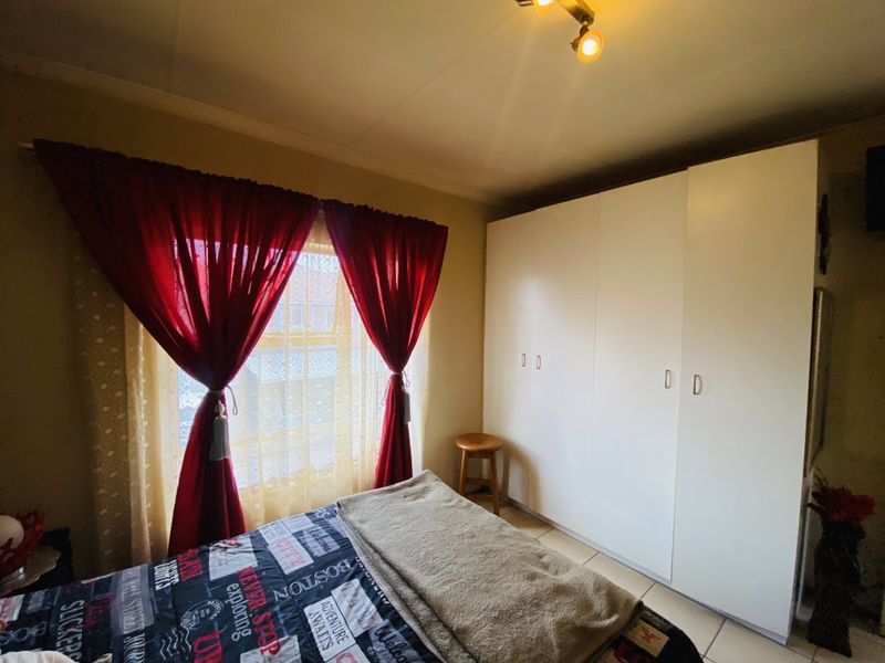 A bedroom featuring a large white built-in wardrobe and a window with curtains, providing functional storage space.