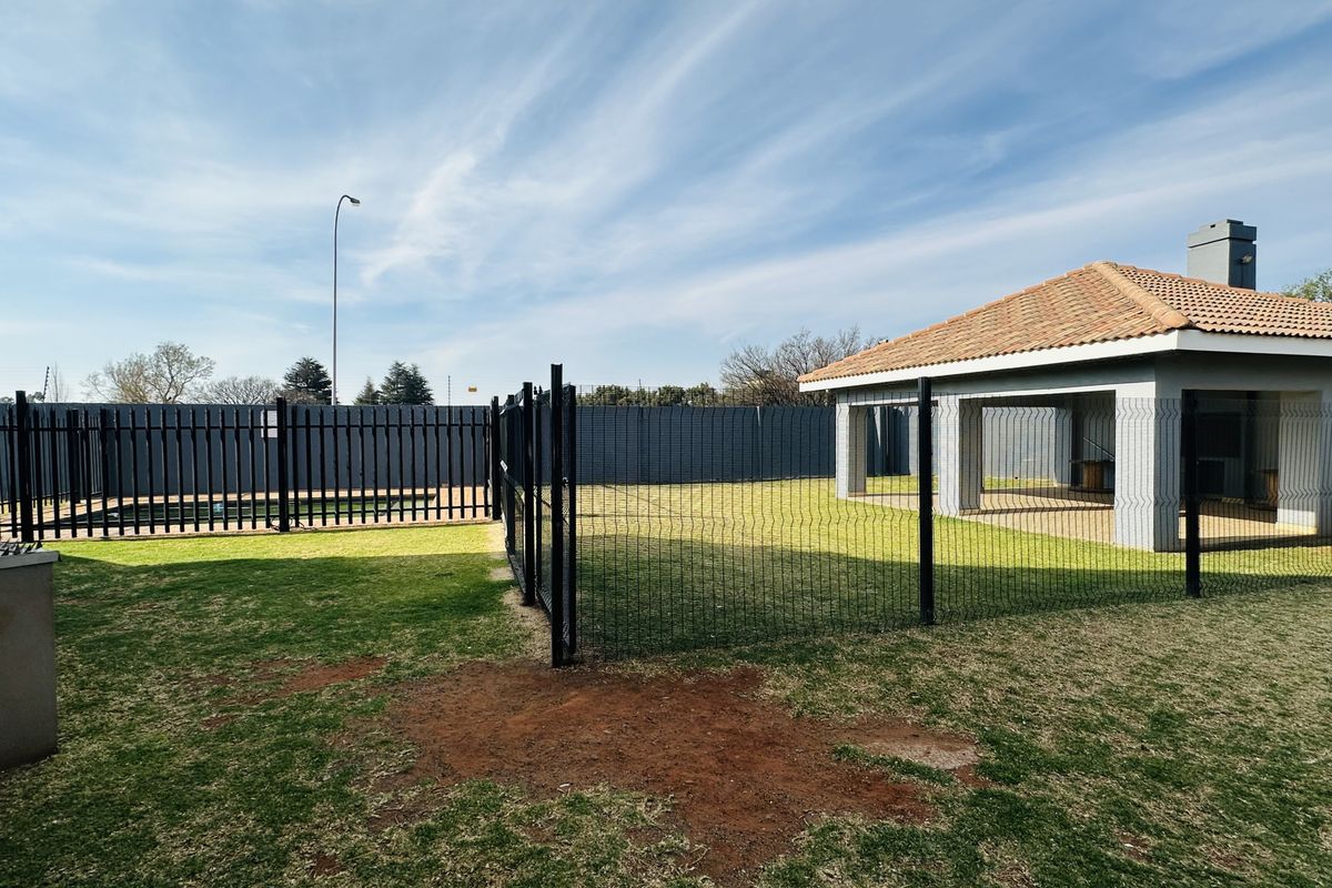 A spacious rear garden area featuring a covered patio with a tiled roof, perimeter fencing, and a well-maintained lawn.