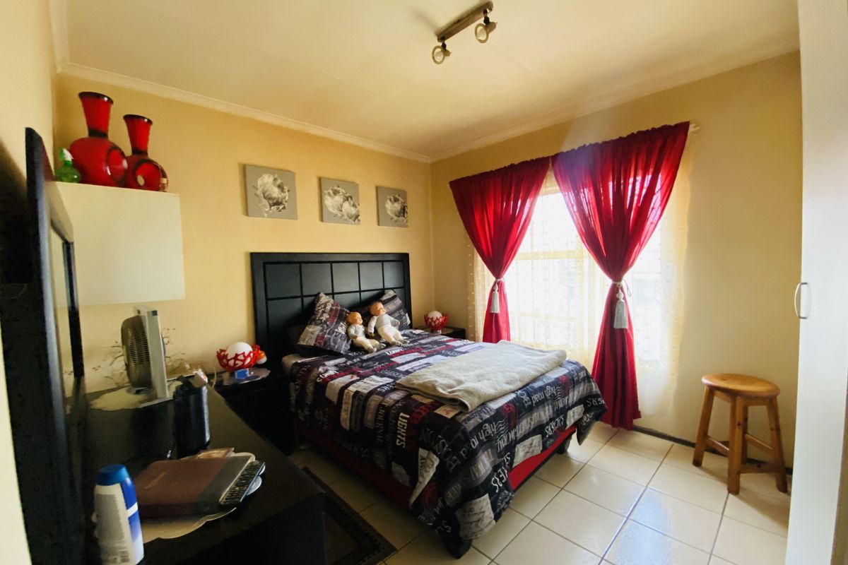 A bedroom featuring tiled flooring, a built-in wardrobe, and natural light through a window with curtains.