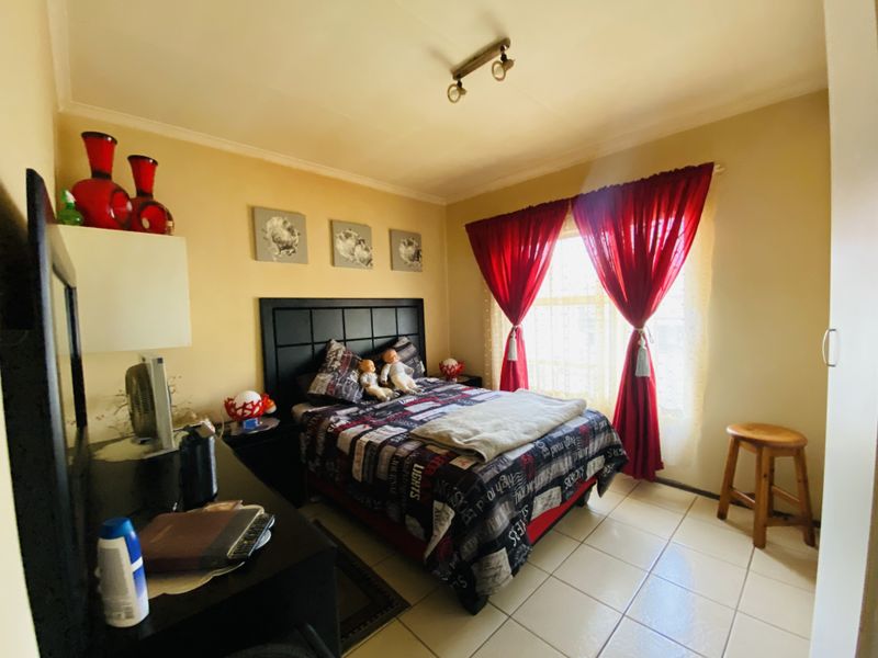 A bedroom featuring tiled flooring, a built-in wardrobe, and natural light through a window with curtains.