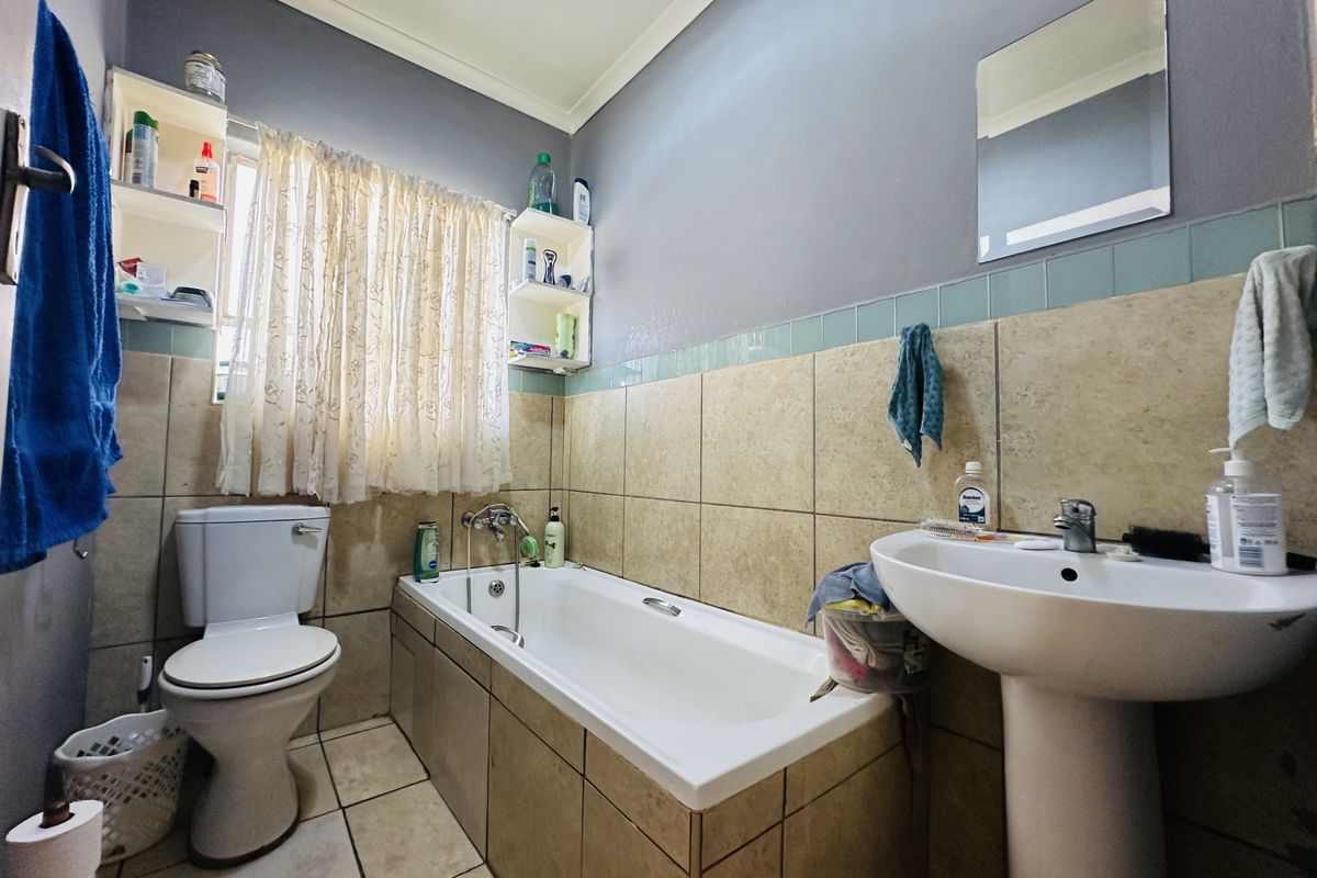 A functional bathroom featuring a pedestal basin, built-in bathtub, and toilet with neutral wall and floor tiling.