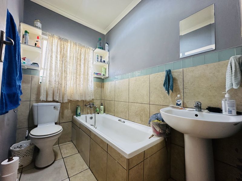 A functional bathroom featuring a pedestal basin, built-in bathtub, and toilet with neutral wall and floor tiling.