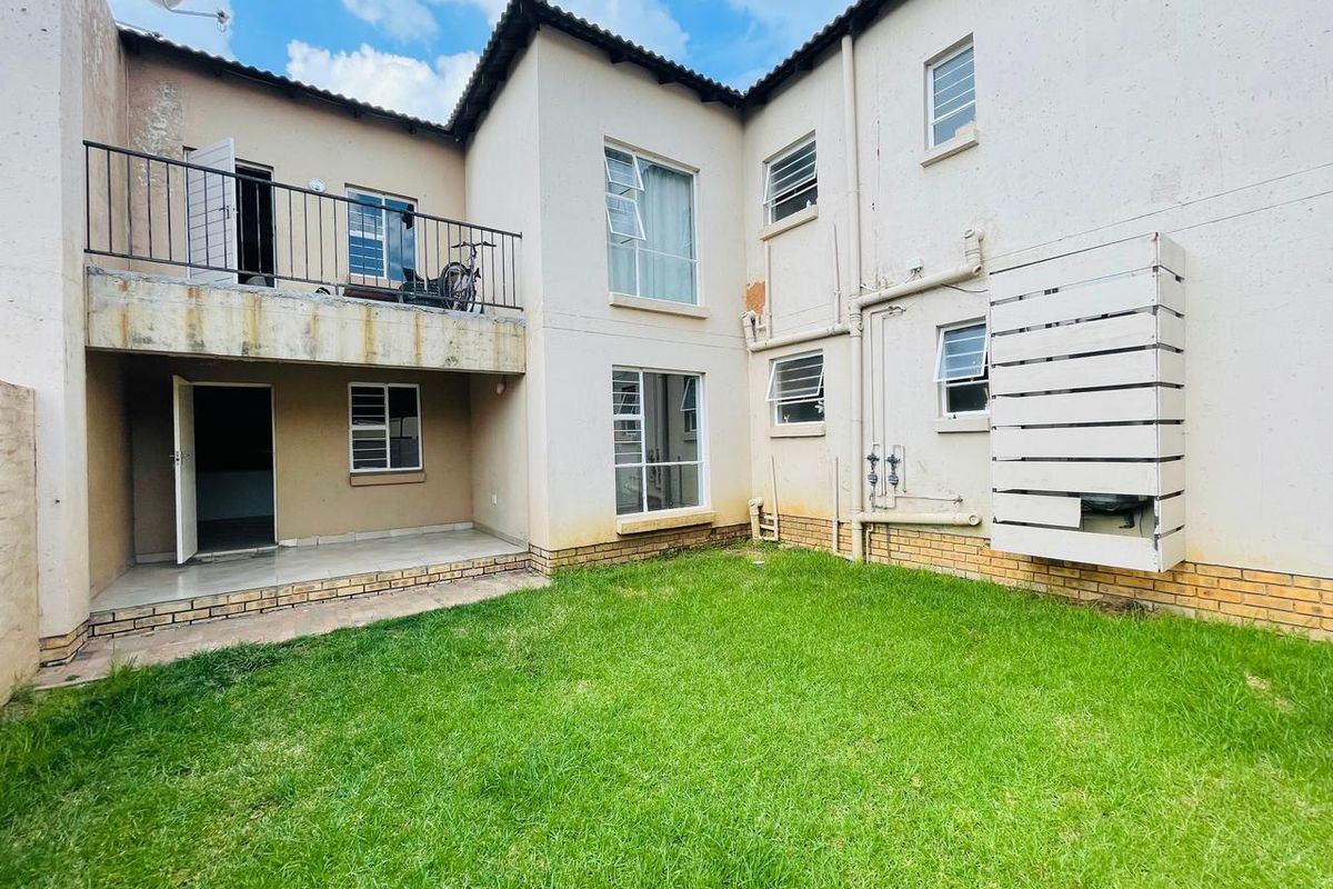 Rear view of the apartment building featuring a small lawn, a ground-floor patio, and an upper-level balcony with metal railings.
