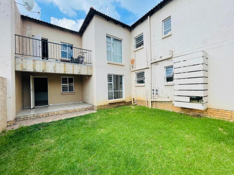 Rear view of the apartment building featuring a small lawn, a ground-floor patio, and an upper-level balcony with metal railings.