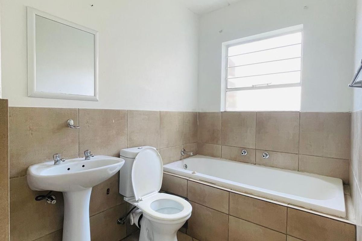 A functional bathroom featuring a pedestal basin, toilet, and built-in bathtub with neutral wall and floor tiling.