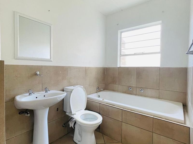 A functional bathroom featuring a pedestal basin, toilet, and built-in bathtub with neutral wall and floor tiling.