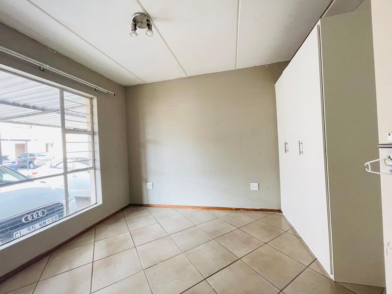 A vacant bedroom featuring tiled flooring, built-in cupboards, and a large window providing natural light.
