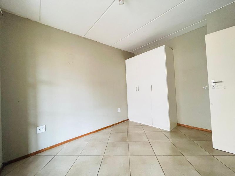 A vacant bedroom featuring neutral wall tones, tiled flooring, and a built-in white wardrobe, offering a clean canvas for personalization.