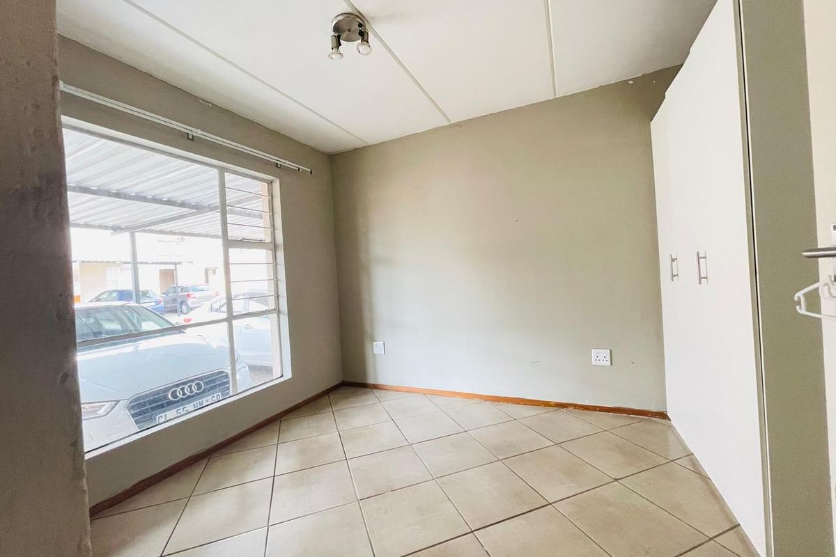 A vacant bedroom featuring tiled flooring, built-in cupboards, and a large window providing natural light.