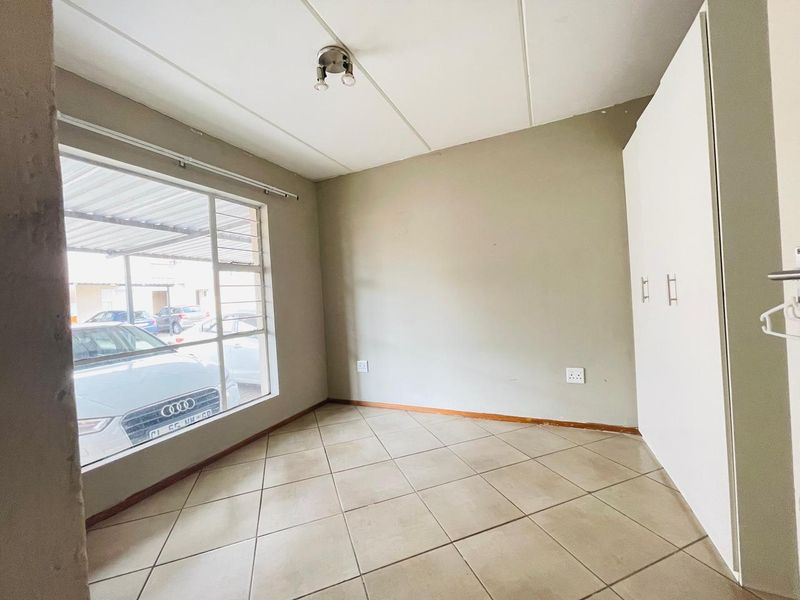 A vacant bedroom featuring tiled flooring, built-in cupboards, and a large window providing natural light.