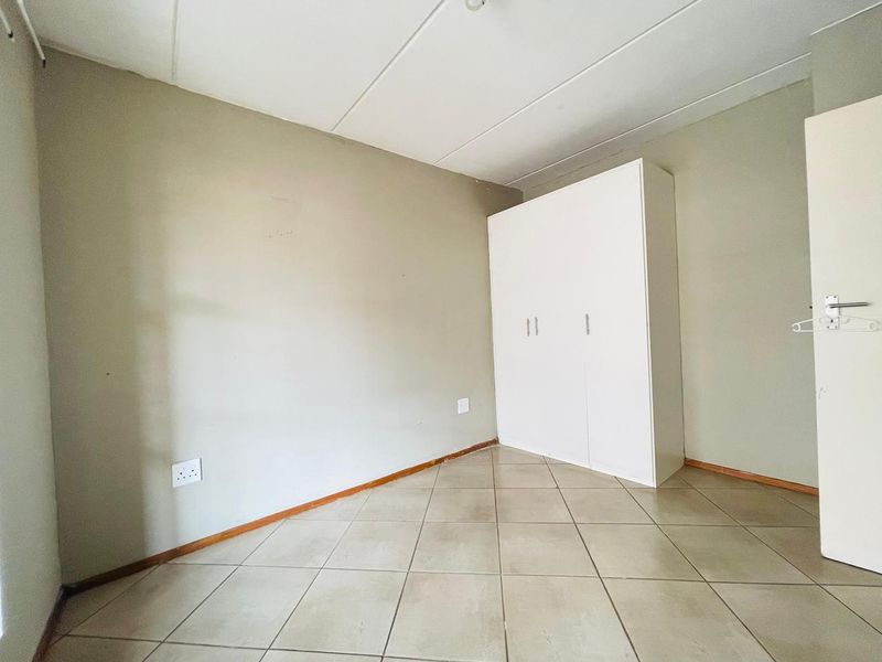 A vacant bedroom featuring neutral wall tones, tiled flooring, and a built-in white wardrobe.