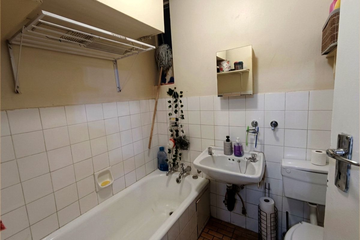 A functional bathroom featuring a standard bathtub, wall-mounted basin, and toilet with tiled splashbacks and a wall-mounted drying rack.