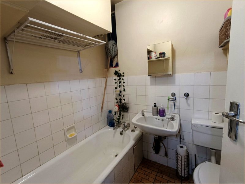 A functional bathroom featuring a standard bathtub, wall-mounted basin, and toilet with tiled splashbacks and a wall-mounted drying rack.