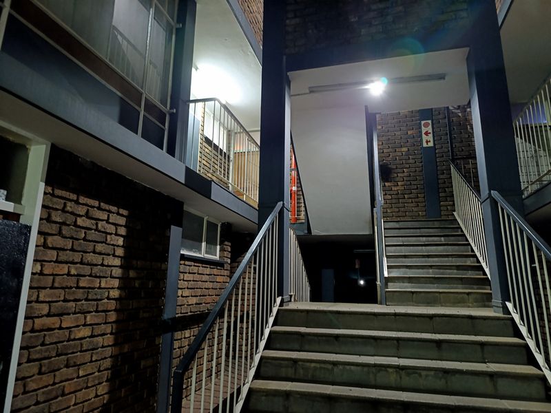 Exterior view of an apartment building staircase and walkway at night, featuring exposed brickwork and metal safety railings.